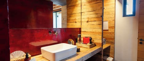 Un baño con tocador de madera, lavamanos blanco y pared roja.