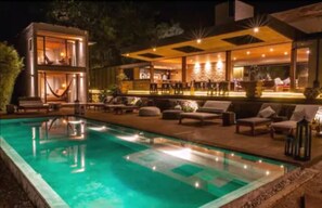 Un espace piscine extérieur moderne, doté de chaises longues et d’un bar.