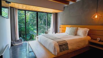 Un dormitorio moderno con una cama grande, cabecera de madera y vistas a la vegetación a través de ventanas de gran altura.