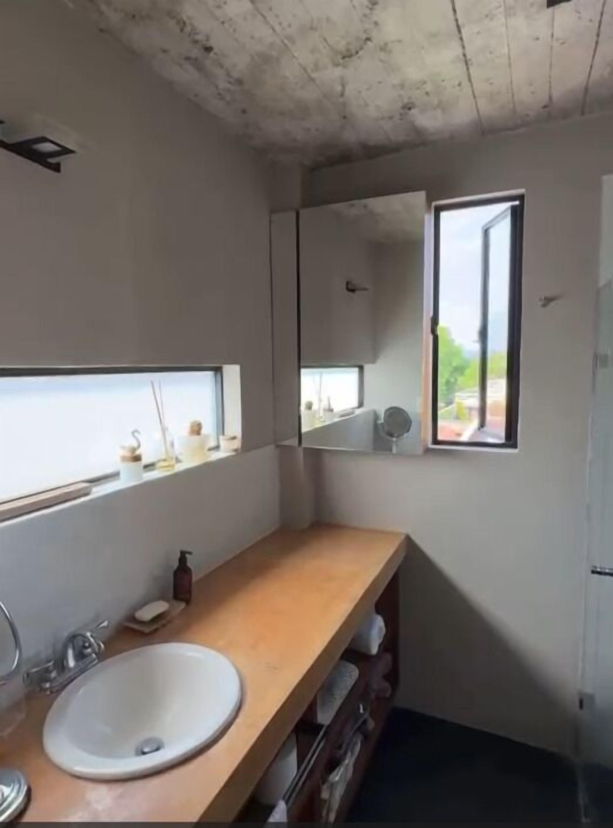 A bathroom with a wooden vanity, a white sink, a mirror, and a window providing a view of the outdoors.