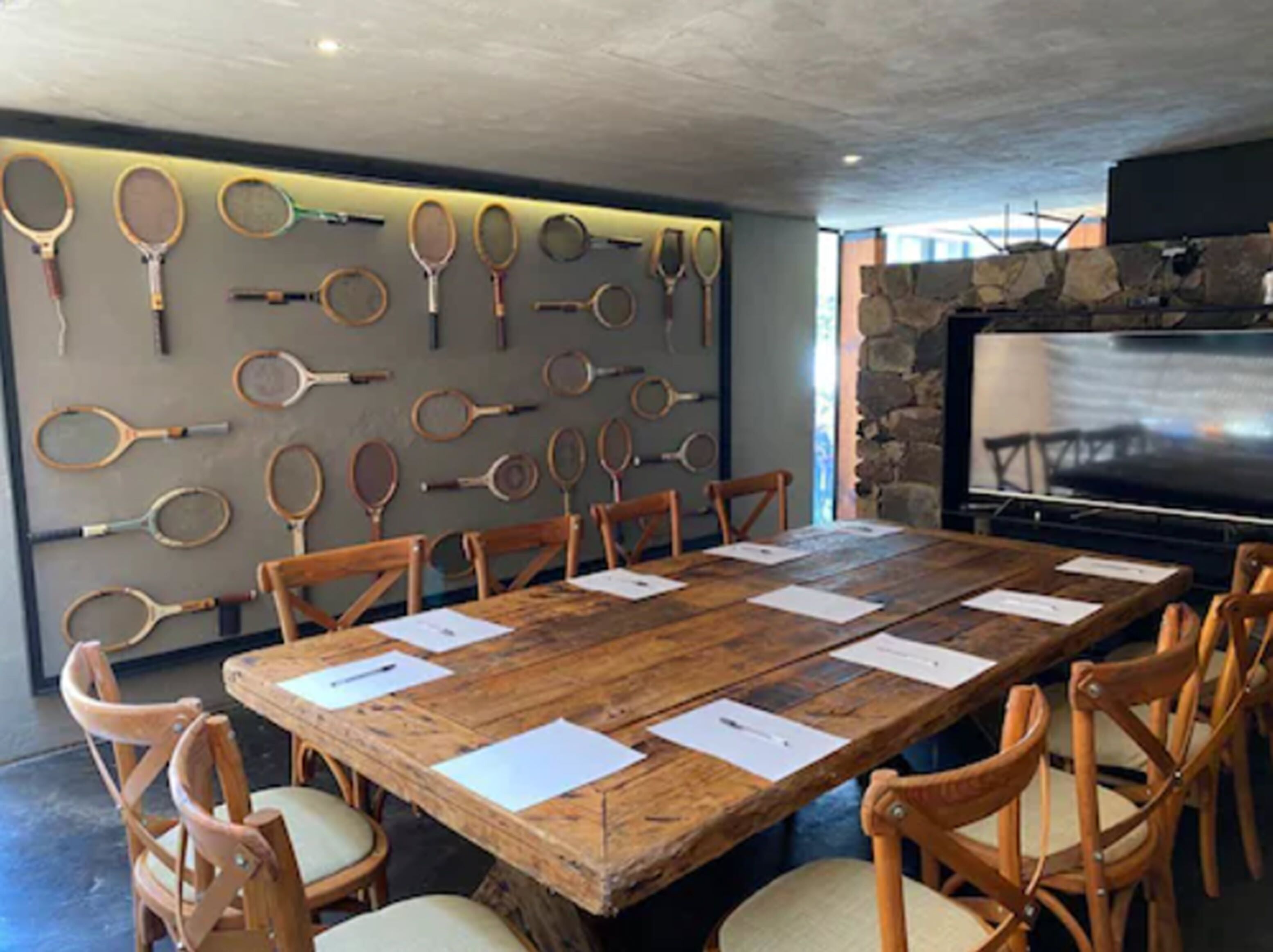 A conference room with a long wooden table, wooden chairs, and a wall displaying various tennis rackets.
