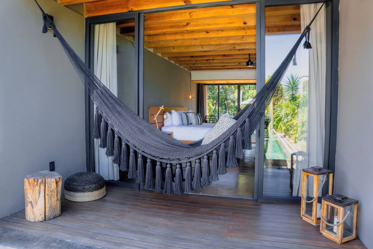 A hammock on a wooden deck with a bed and a view of greenery.