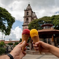 Deux cornets de glace sont tenus devant un bâtiment historique doté d’un clocher.