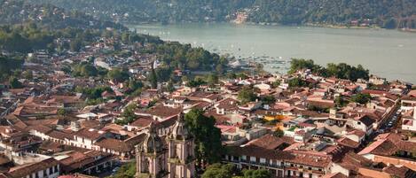 Un pueblo histórico con una iglesia destacada que presenta un campanario, rodeado de edificios con tejas rojas y un lago al fondo.