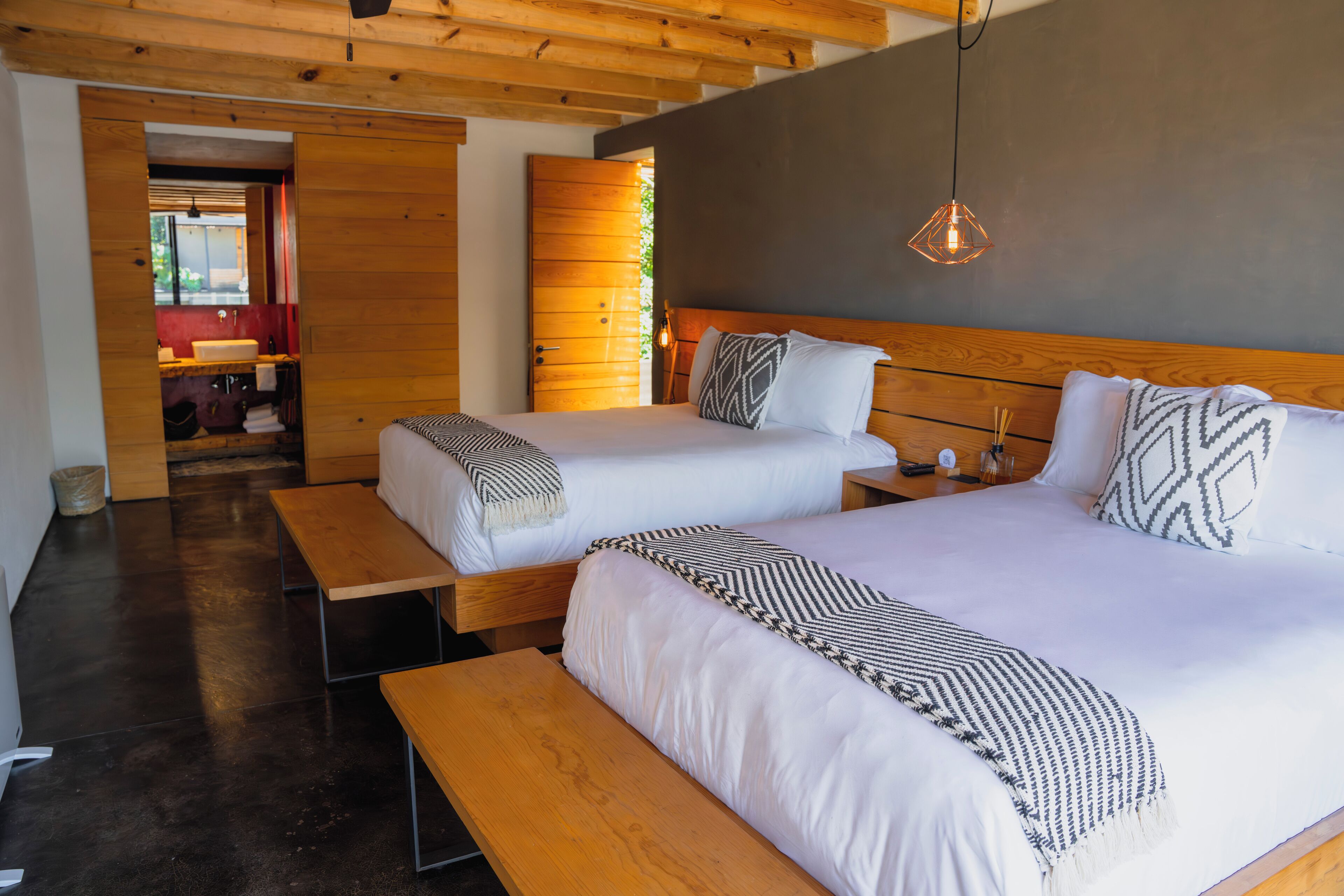 Een moderne hotelkamer met twee bedden, houten vloeren, een bankje en een groot raam.