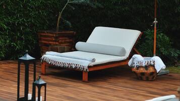 Una terraza de madera con dos sillones de descanso y una sombrilla.