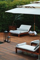 Una terraza de madera con dos sillones de descanso y una sombrilla.