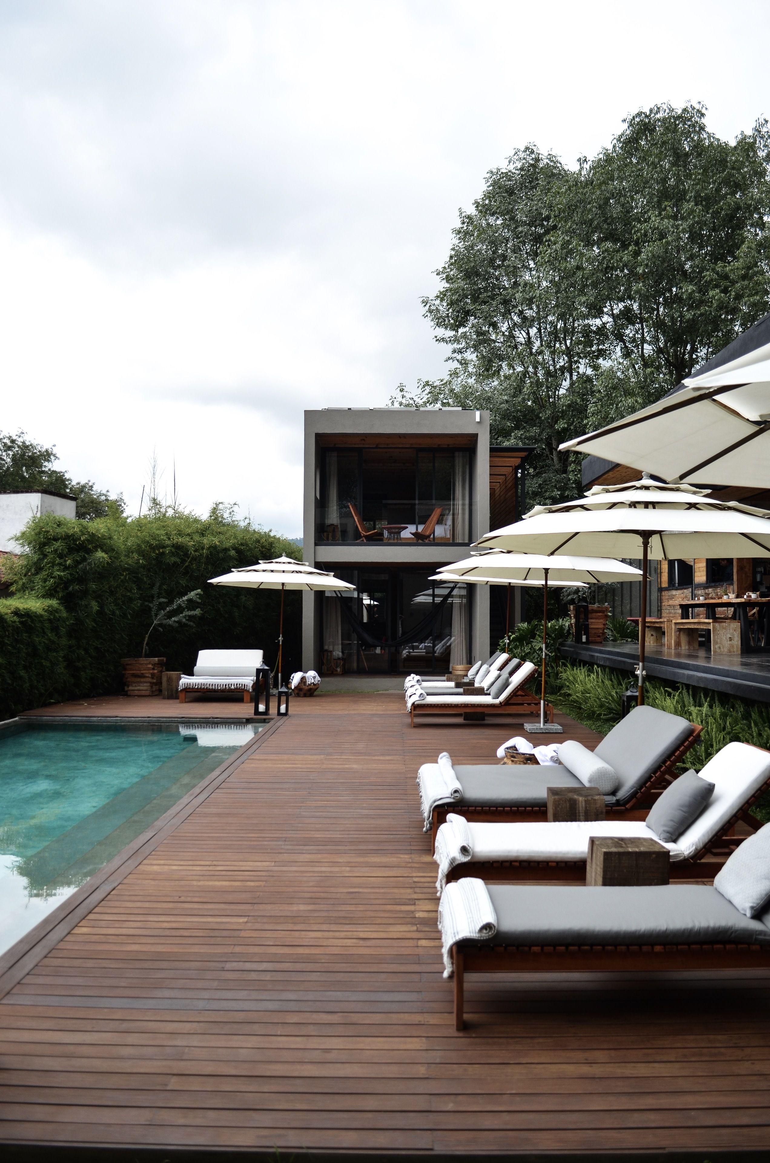 A wooden deck with lounge chairs and umbrellas, a pool, and a modern building with a balcony.
