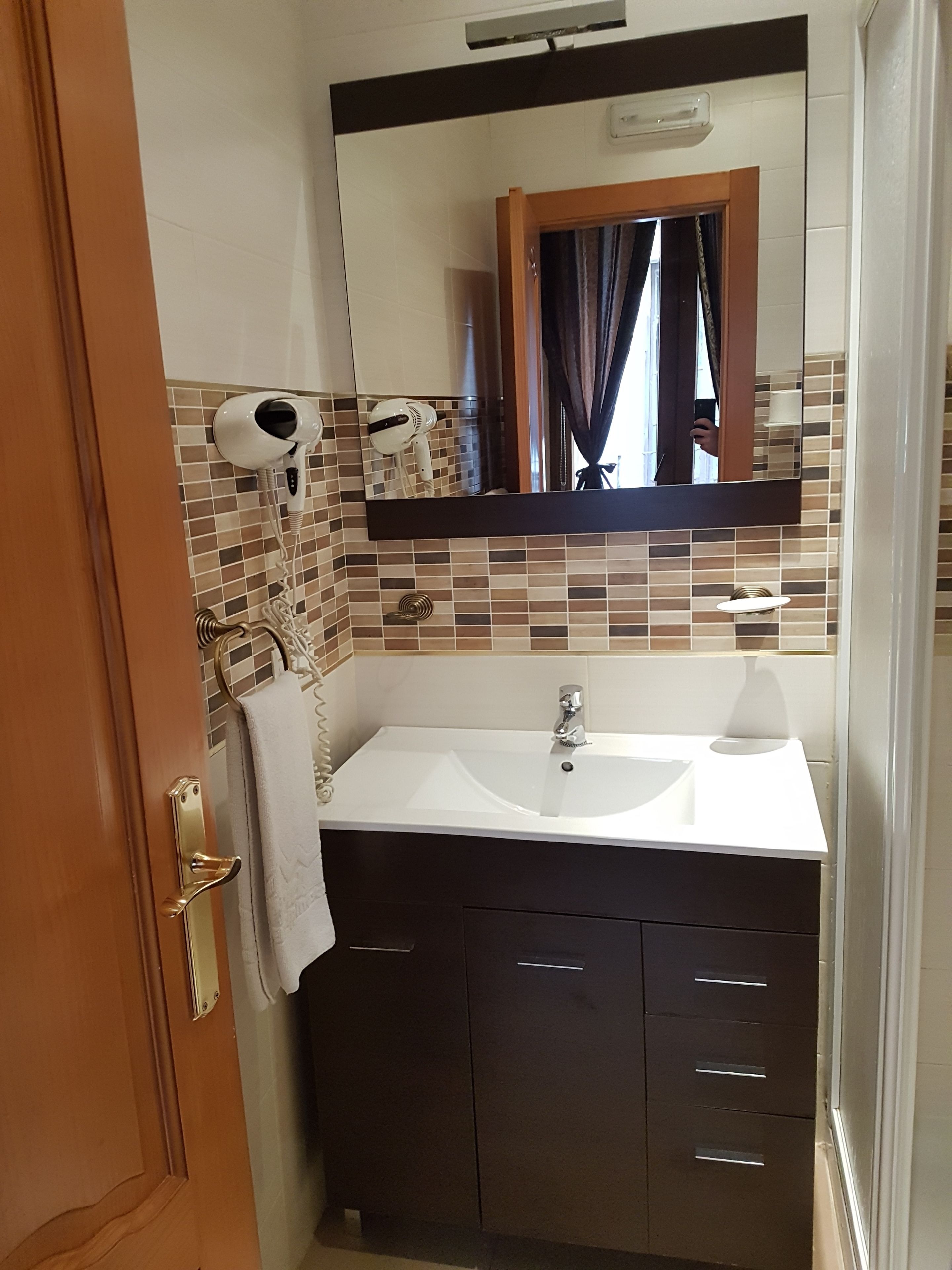 A bathroom with a white sink, dark cabinets, a towel rack, and two hair dryers mounted on the wall.