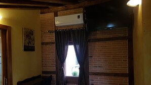 Ein Zimmer mit Backsteinwand, einem Vorhangfenster, einer Holzbank, einem kleinen Tisch und einer Klimaanlage.
