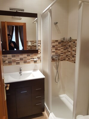 A bathroom with a white sink, dark cabinets, a mirror, and a shower area with tiled walls. - Hostal Segovia (Segovia)