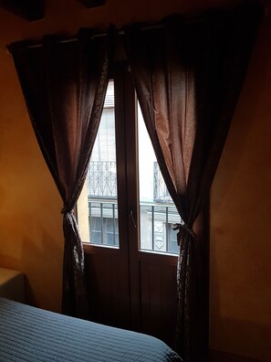 A room with a bed, a window with curtains, and a view of buildings outside. - Hostal Segovia (Segovia)
