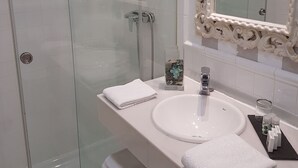 Ein Badezimmer mit Duschkabine aus Glas, einem weißen Waschbecken und einem dekorativen Spiegel.