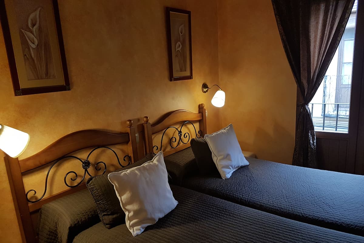 A double bed with a wooden headboard, two pillows, and a quilted bedspread. There are wall-mounted light fixtures and two framed floral artworks above the bed.