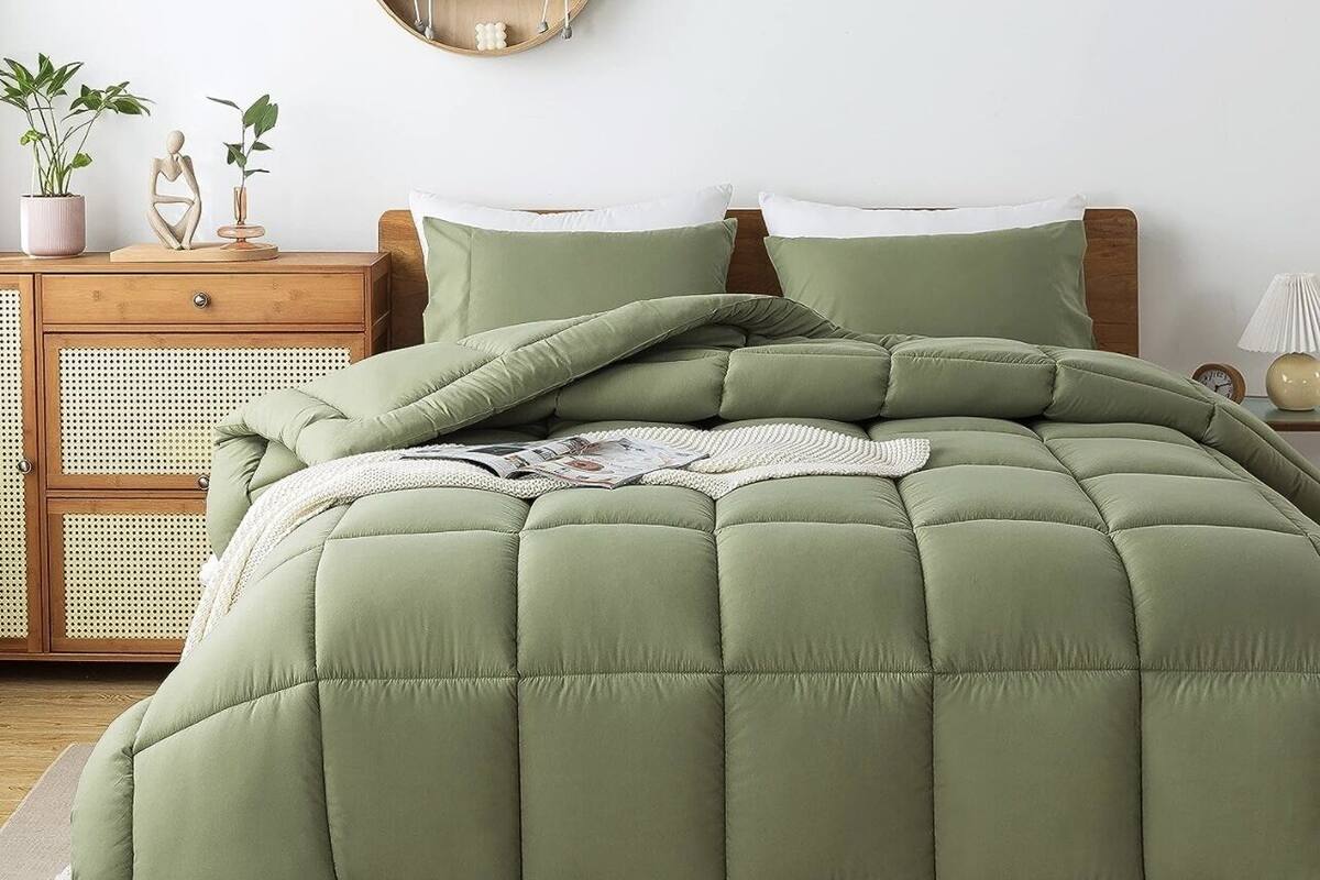 A bed with a green quilt, a wooden nightstand with a lamp, and a wall-mounted shelf with plants.