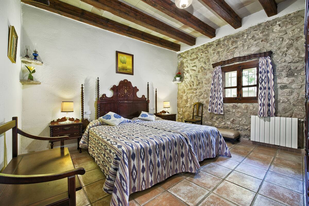 A bedroom with a large bed, wooden headboard, stone walls, and a rustic wooden ceiling.