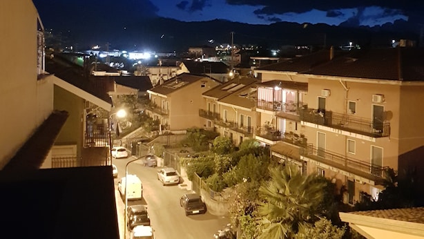 A nighttime view of a street with parked cars and buildings. - B&B Mimosa (Giardini Naxos)