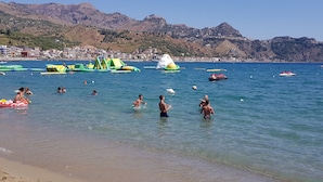 A beach with clear water, people swimming and playing, and inflatable structures. - B&B Mimosa (Giardini Naxos)