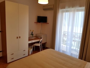Habitación de hotel con cama, escritorio con silla, televisor en la pared y ventana con cortinas.