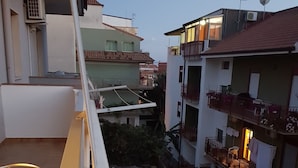 A balcony with a metal chair and a small table, overlooking a residential area with buildings and a narrow street. - B&B Mimosa (Giardini Naxos)