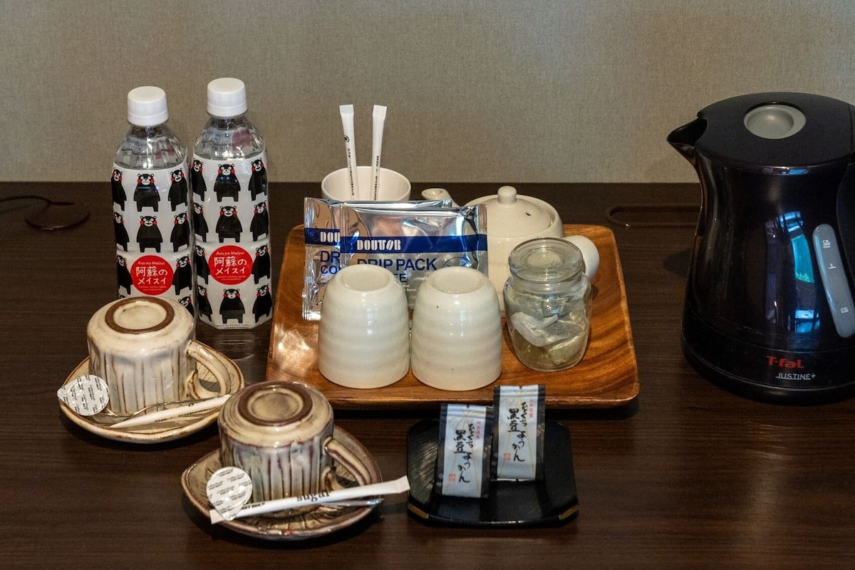 A table with various items including bottles, a coffee maker, sugar packets, and a tea set.
