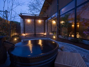 Un área moderna de hidromasaje al aire libre con una terraza de madera, suelo de piedra y una pérgola de madera.