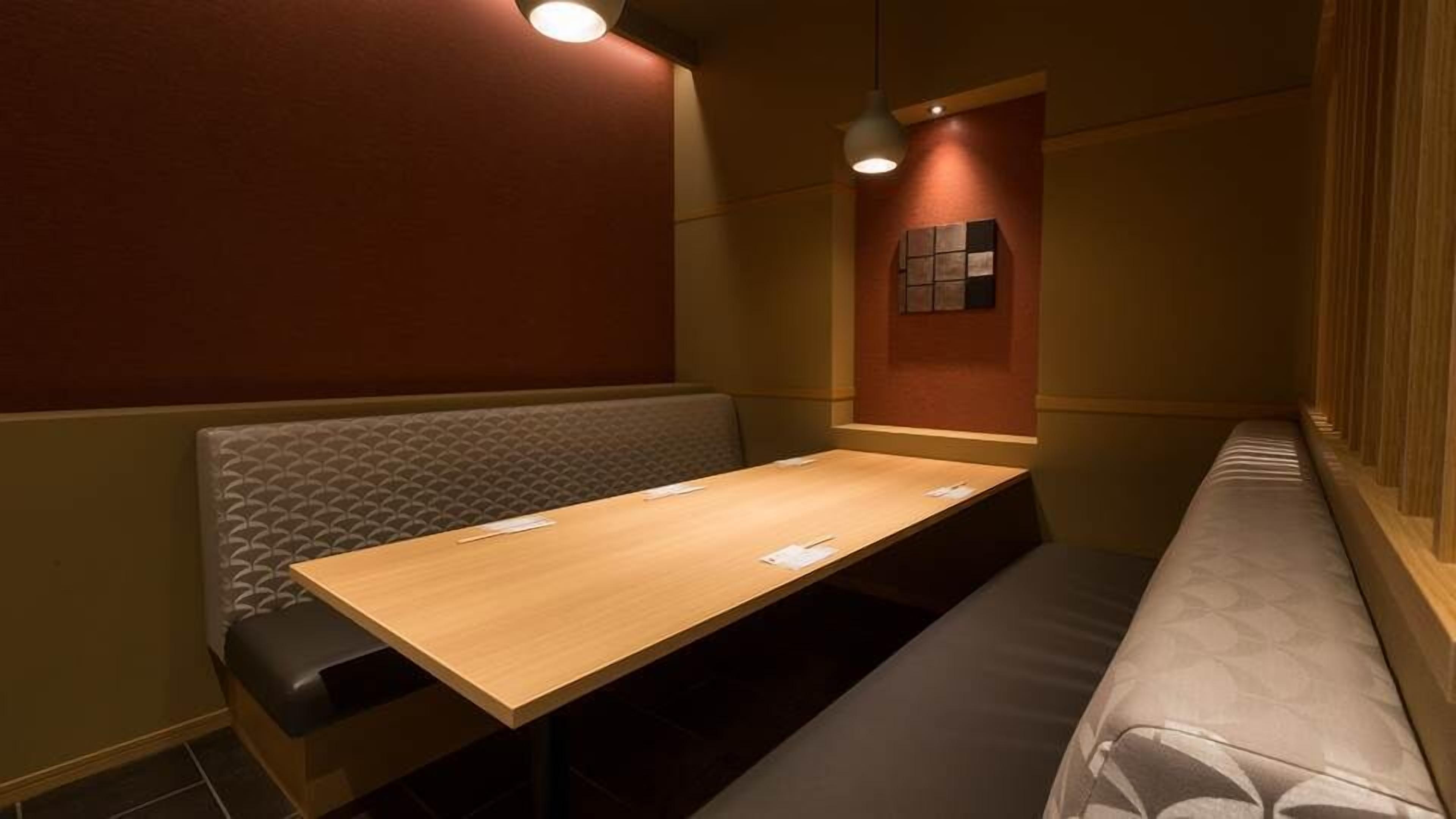 Una habitación pequeña y privada con una mesa de madera, dos bancos acolchados y una lámpara fijada a la pared.