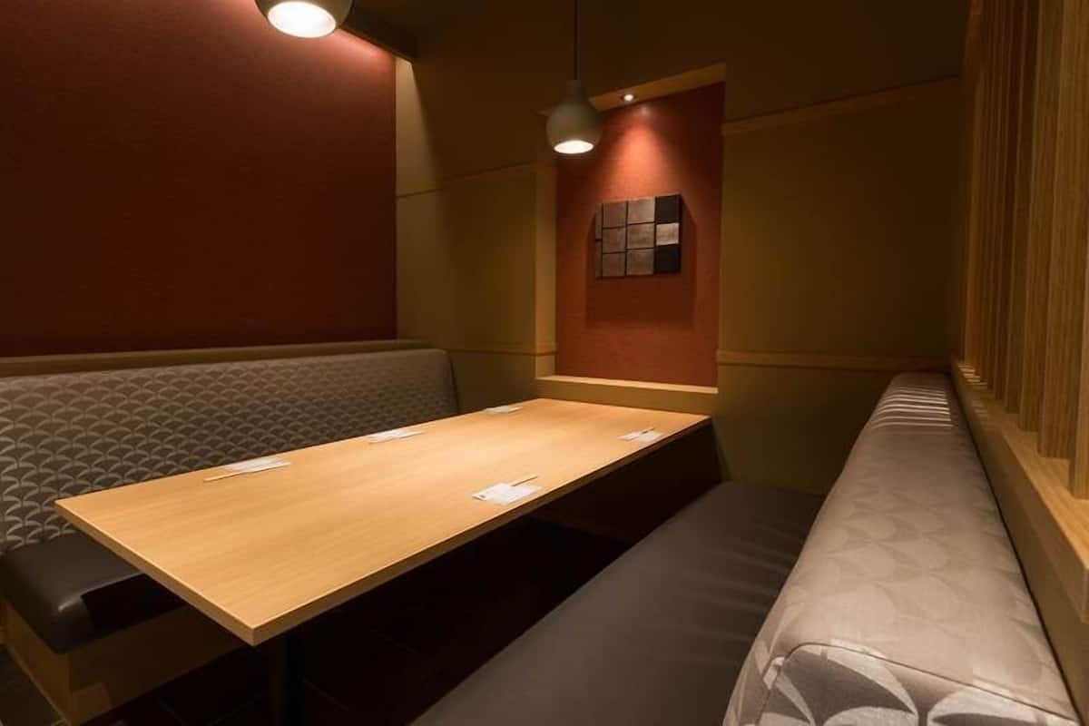 A small, private room with a wooden table, two cushioned benches, and a wall-mounted light fixture.