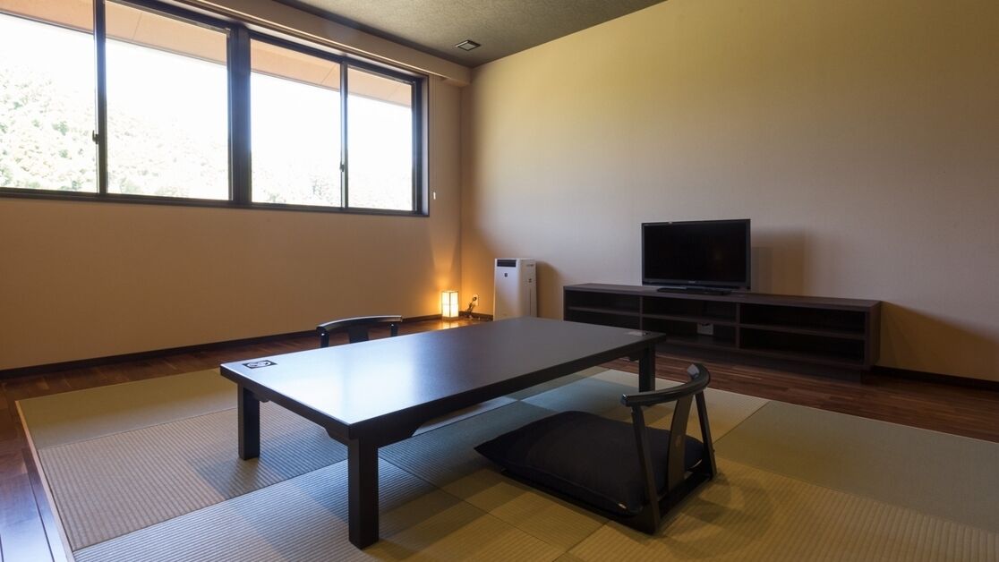Una habitación con suelo de tatami, una mesa baja, una silla negra, un televisor y un calefactor.