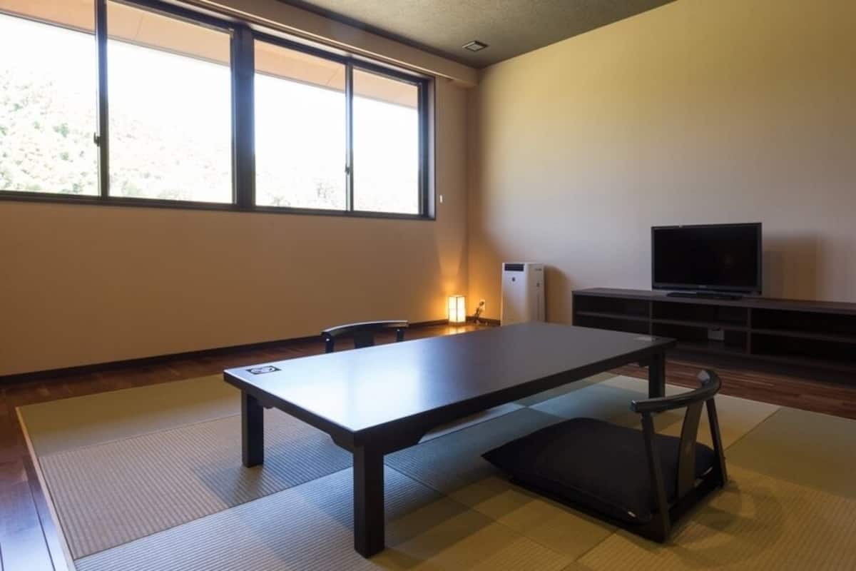 A room with tatami flooring, a low table, a black chair, a television, and a heater.