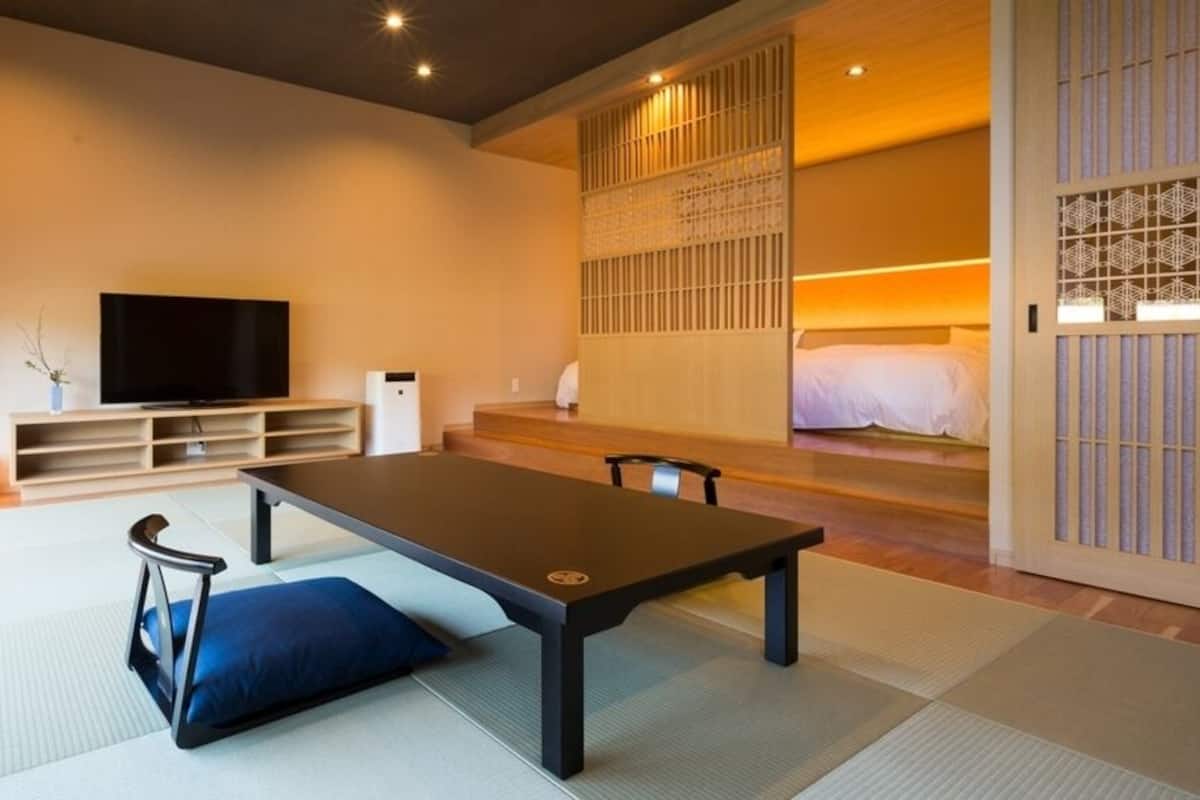 A modern room with tatami flooring, a low table, a television, and a bed with a wooden headboard.