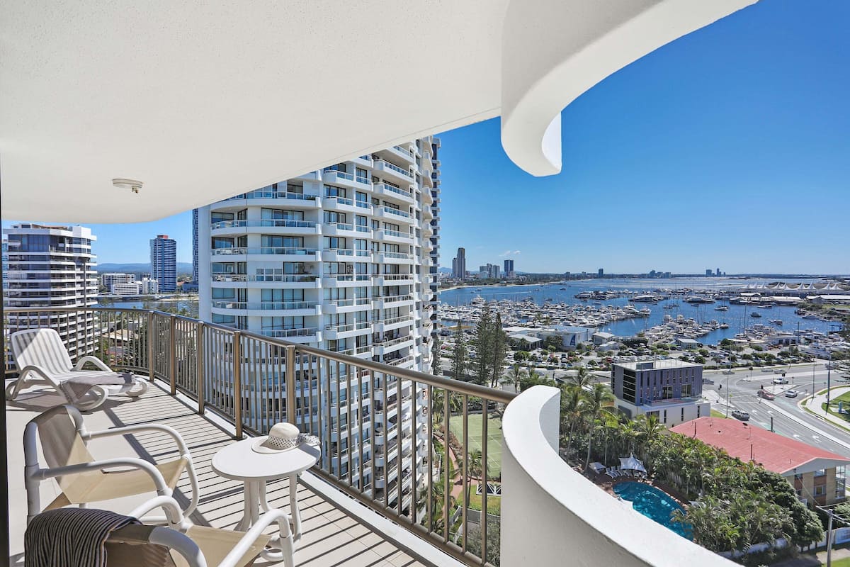 Ein Balkon mit Sitzgelegenheit im Freien, Blick auf einen Yachthafen und hohe Gebäude im Hintergrund.