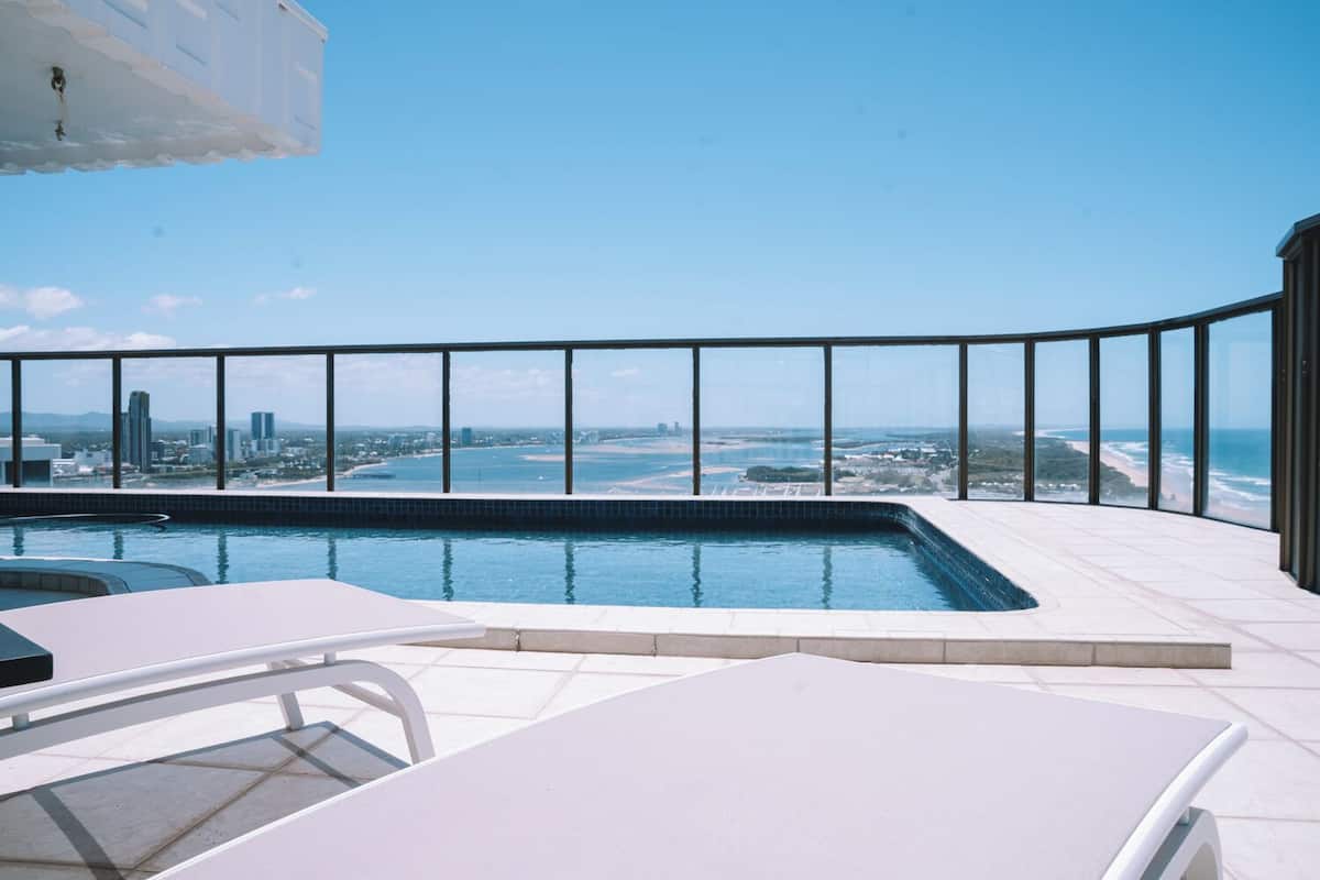 Ein Pool auf dem Dach mit Blick auf die Stadt, einer Lounge und einem Glasgeländer.