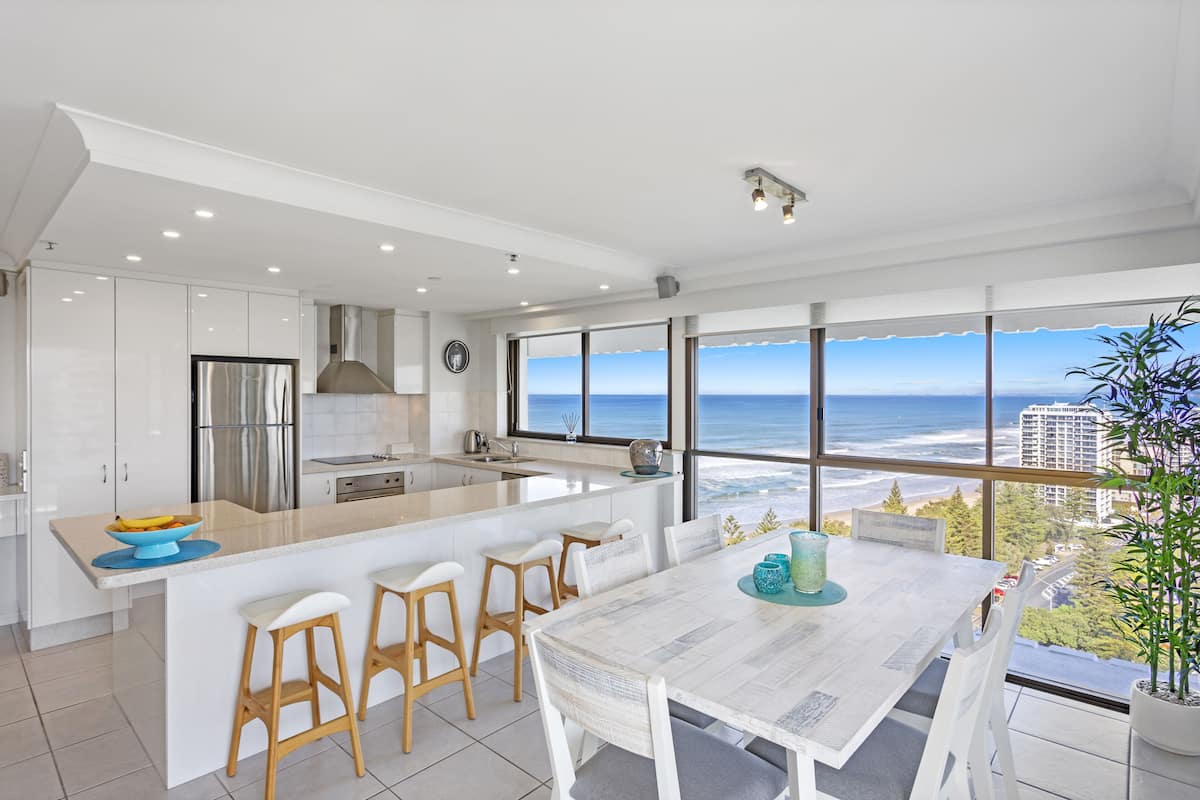 Eine moderne Küche mit einer großen Kochinsel, einem Essbereich mit Meerblick und einem großen Fenster zur Strandpromenade.