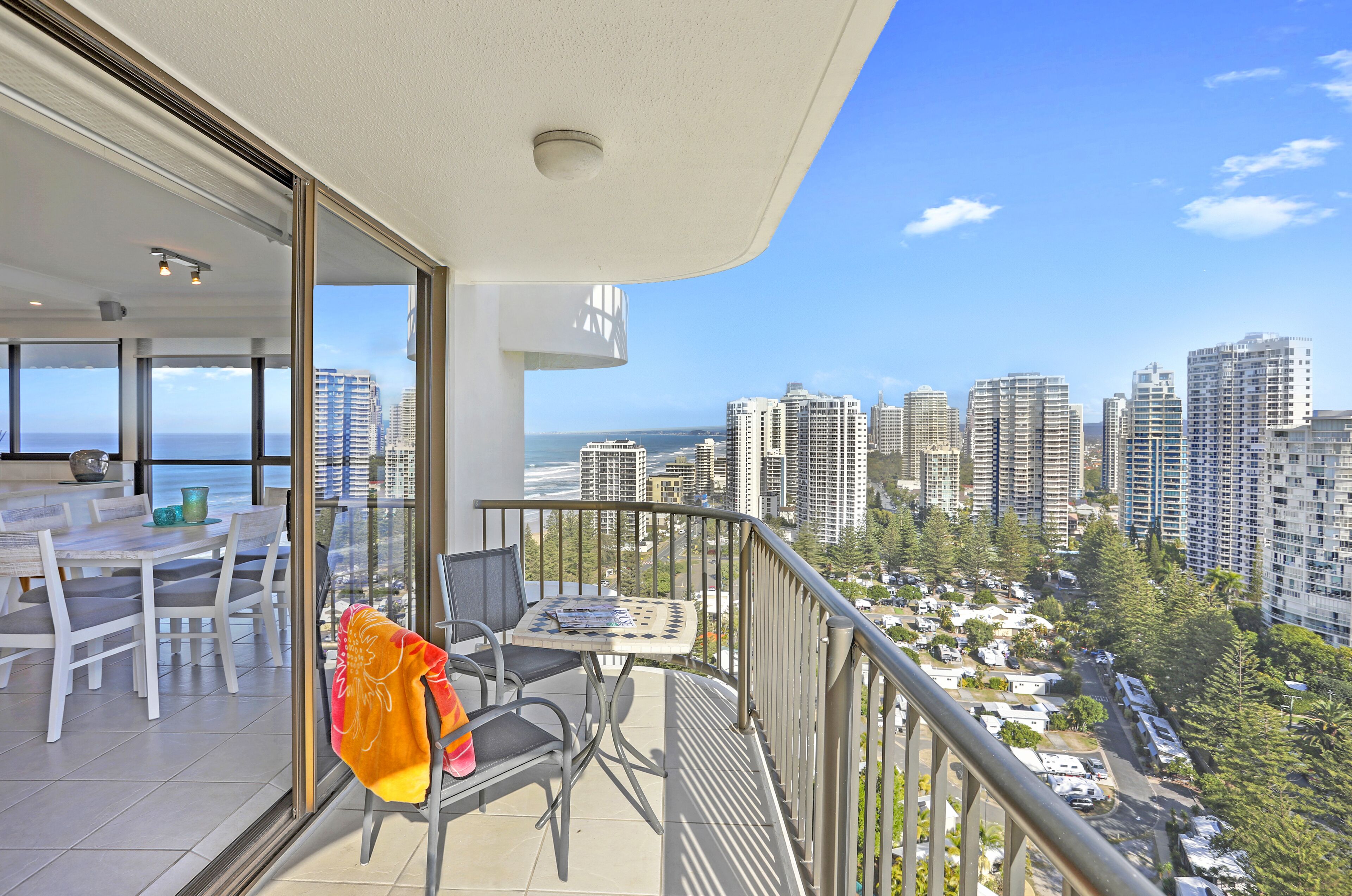 Un balcon avec une table et des chaises, donnant sur un paysage urbain avec de hauts immeubles et une vue sur la mer.