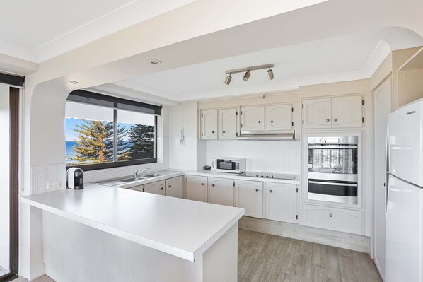 A modern kitchen with white cabinetry, a large island, a microwave, an oven, and a refrigerator.