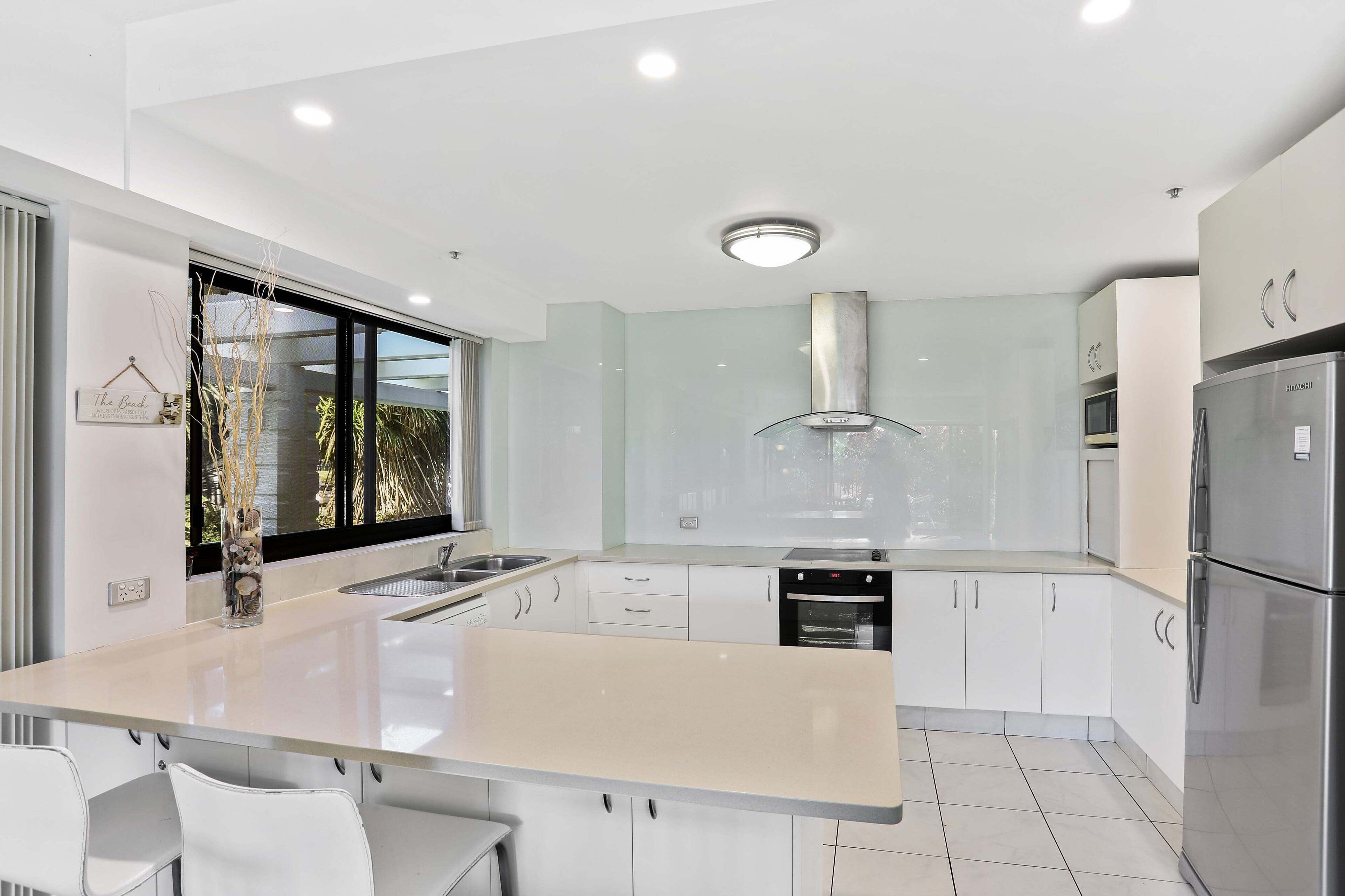 Una cocina moderna con una isla central, electrodomésticos de acero inoxidable y vistas al exterior.
