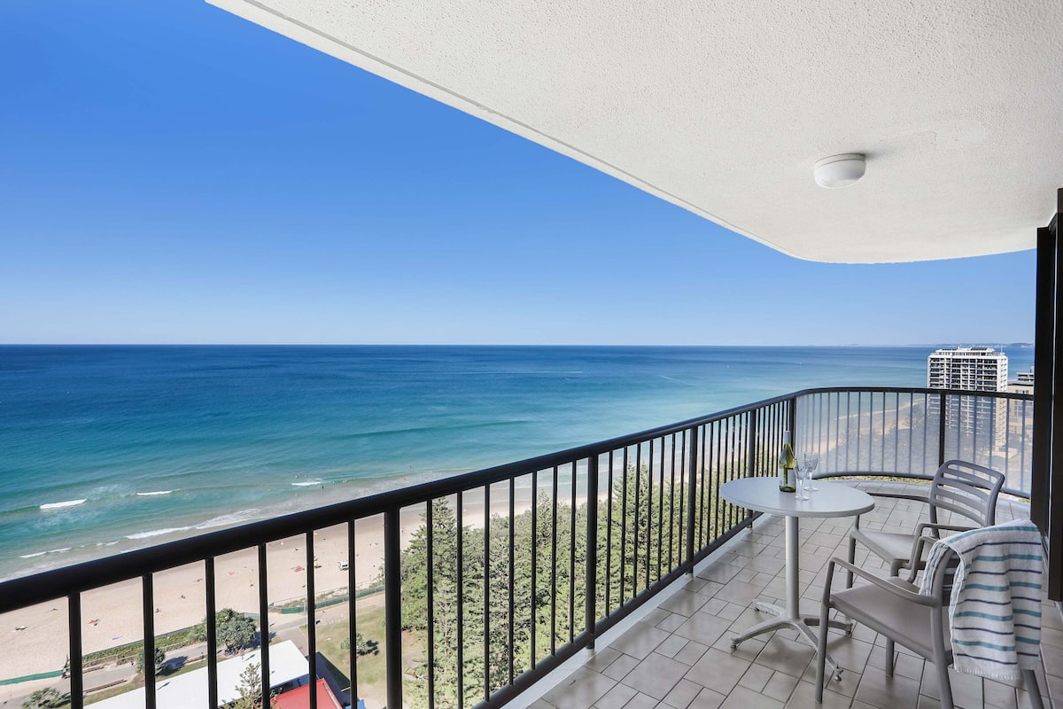 Ein Balkon mit Blick auf das Meer und den Strand, einem Tisch mit Stühlen und einer Brüstung.