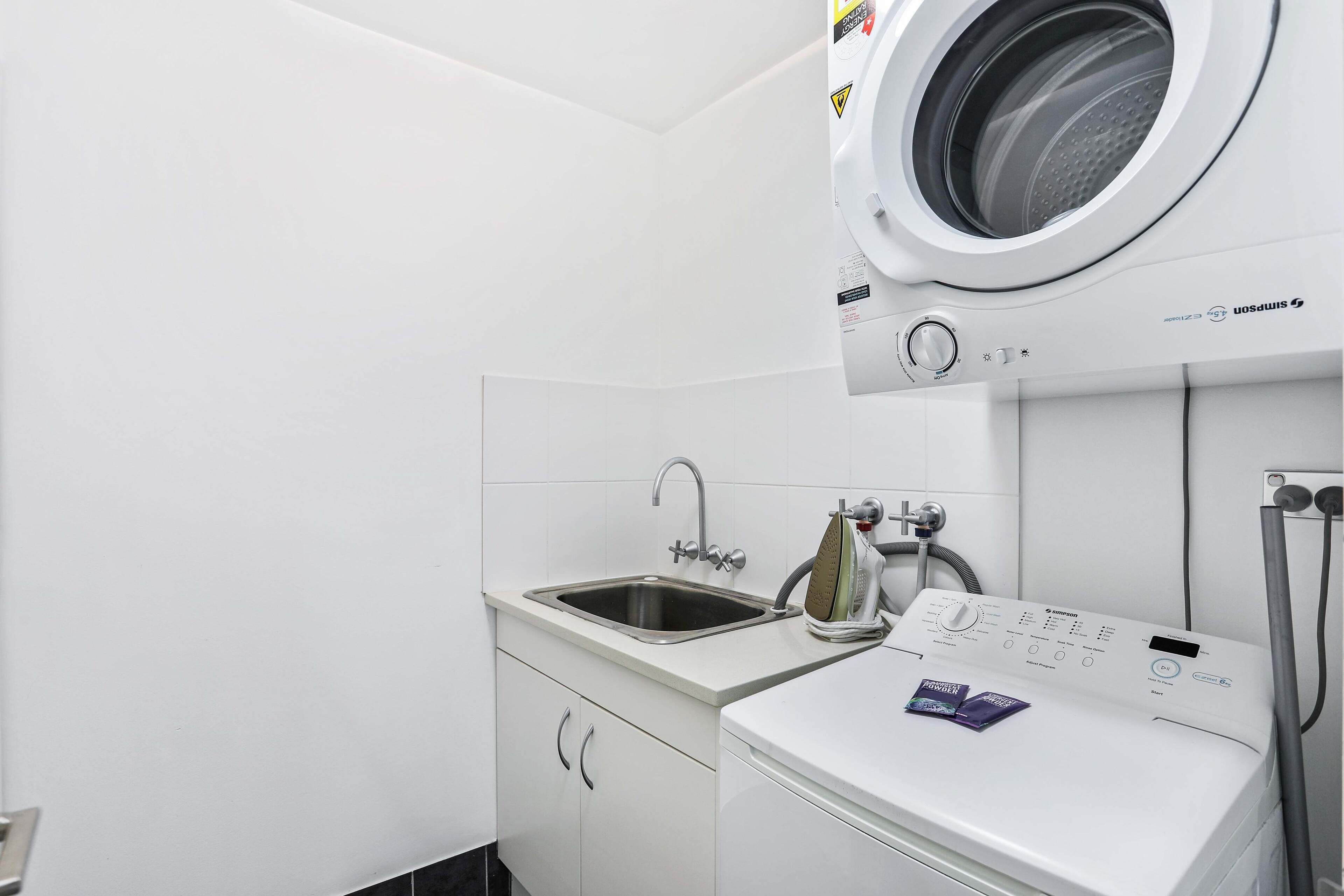 Un lavadero pequeño y funcional, con lavadora y secadora integradas, un lavabo y un armario.
