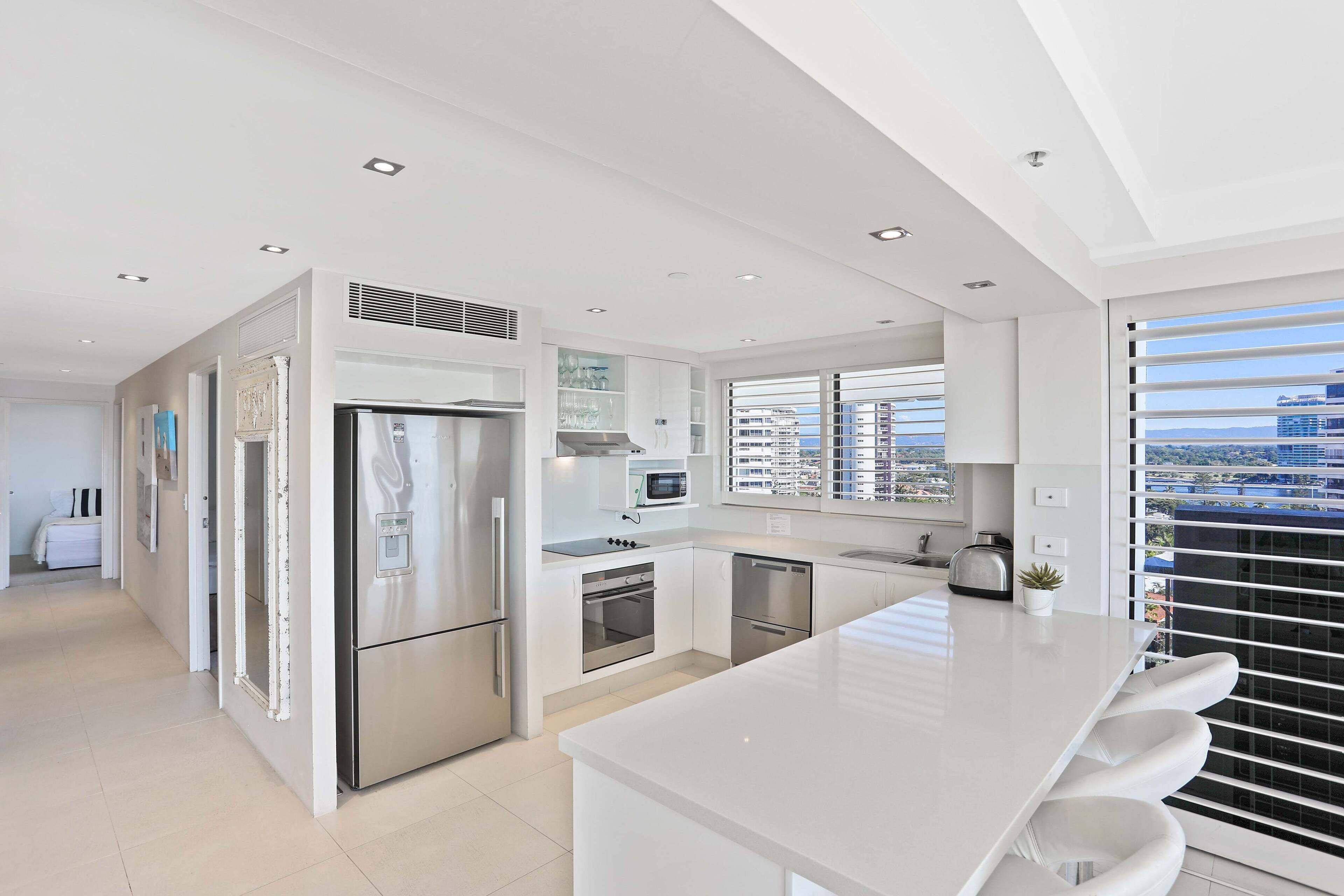 A modern kitchen with white cabinetry, stainless steel appliances, and a large island with bar stools.