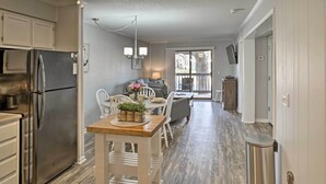 A modern kitchen with a stainless steel refrigerator, a dining area with a wooden table and chairs, and a view of the outdoors through a large window. - Hilton Head Condo w/ Pool Bar: Walk to Beach! (Hilton Head Island)