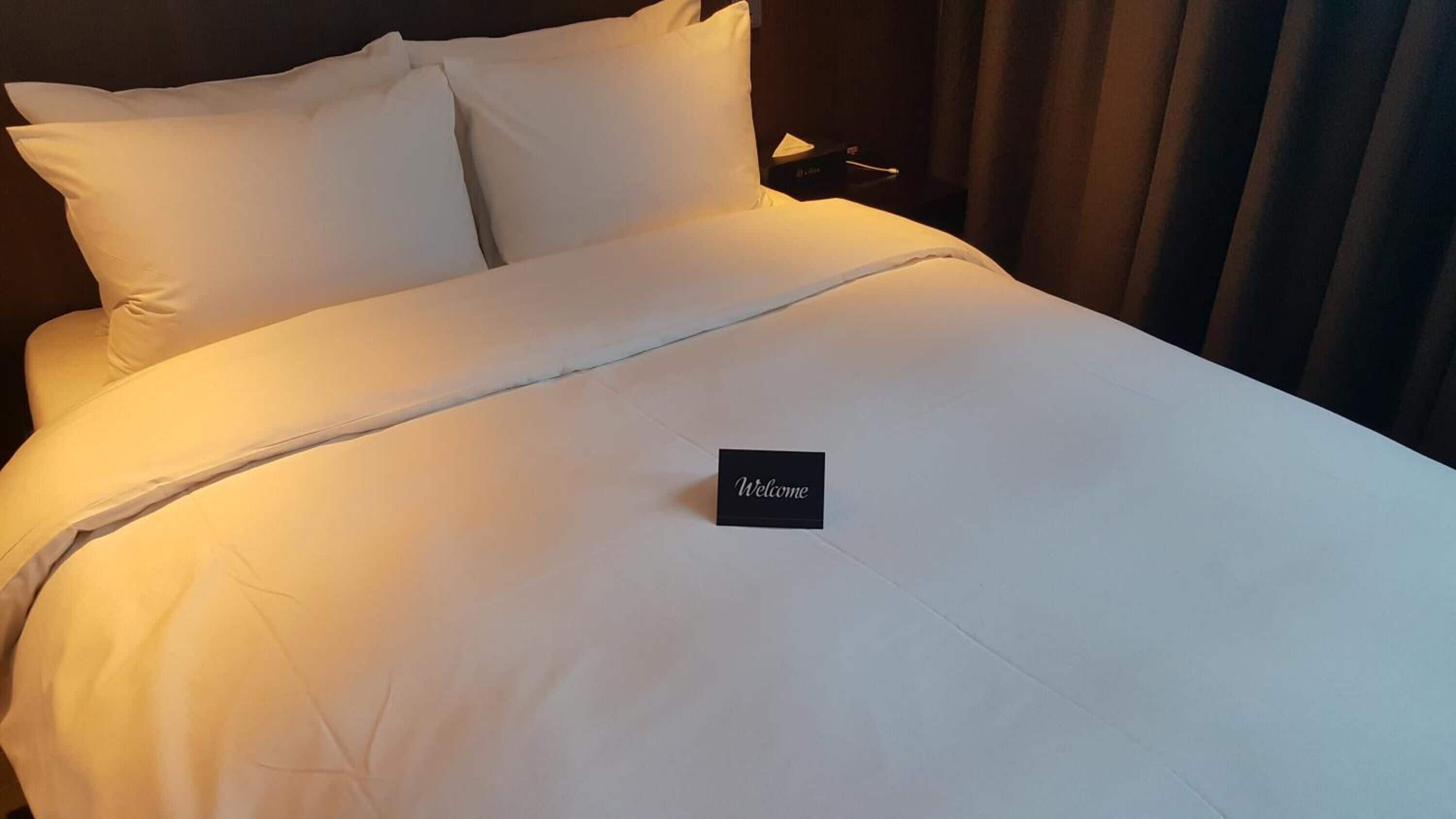 A neatly made bed with white linens and a "Welcome" sign on the bedspread.