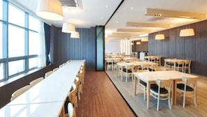 Un comedor moderno con mesas y sillas largas, ventanas amplias e iluminación colgante.