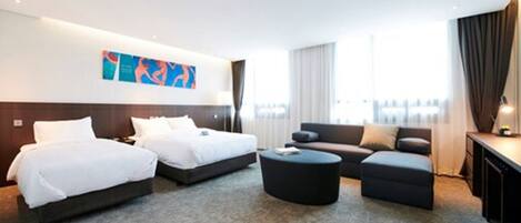 A hotel room with two beds, a sofa, a coffee table, and a desk.
