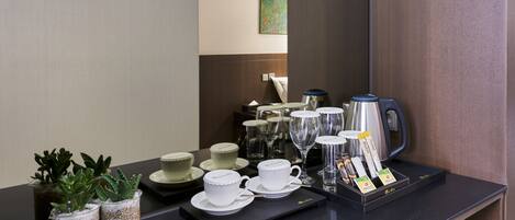 A hotel reception area with a black counter displaying tea cups, a coffee maker, and a tray of tea bags. There are also small potted plants on the counter.