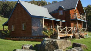 A wooden cabin with a porch and a metal roof, surrounded by rocks and grass. - Fantastic getaway for family or friends with spectacular views. (Snug)