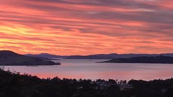 A sunset over a calm lake with surrounding hills and a forested area.