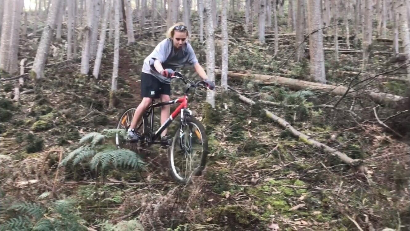 Una persona montando una bicicleta de montaña por un área boscosa con árboles y maleza.