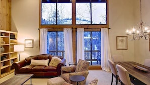 A cozy living room with a leather sofa, patterned armchairs, a wooden coffee table, and a dining table with chairs. Large windows offer a view of a snowy landscape. - Hike In/Out w/Stunning Mountain Views + Heated Pool-Hot Tub-Gym-Wood Fireplace-W/D in Unit (Steamboat Springs)