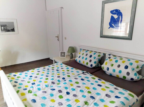 A bedroom with a bed, a nightstand, a lamp, and a door.